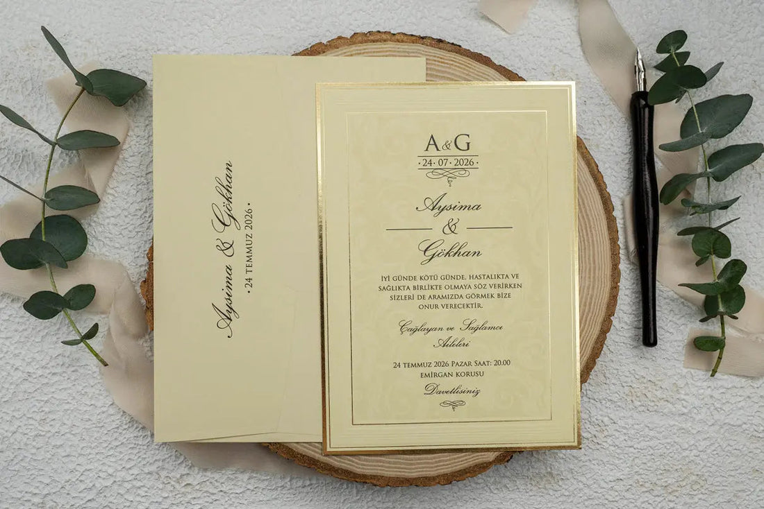 Partecipazione di nozze in carta color crema con bordo dorato accanto alla busta coordinata.