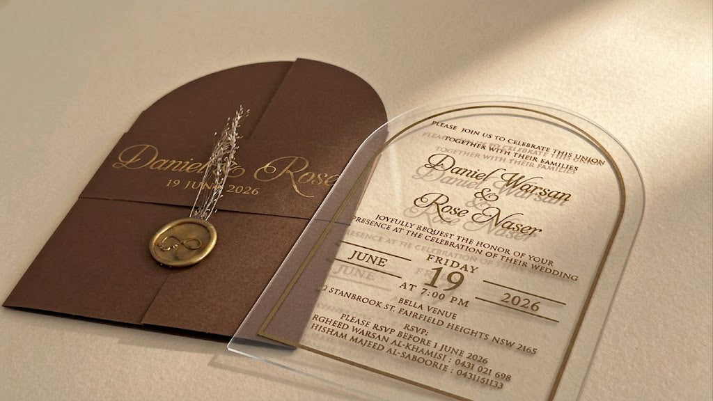 Low view of the brown invitation set showing the clear acrylic card's transparent outer edge and lettering beside the closed cover.