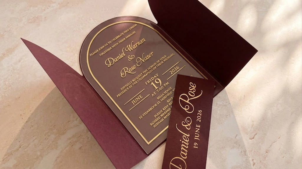 Angled view inside the open burgundy arched gatefold cover, with the clear acrylic invitation centered and the removed printed band across the foreground.