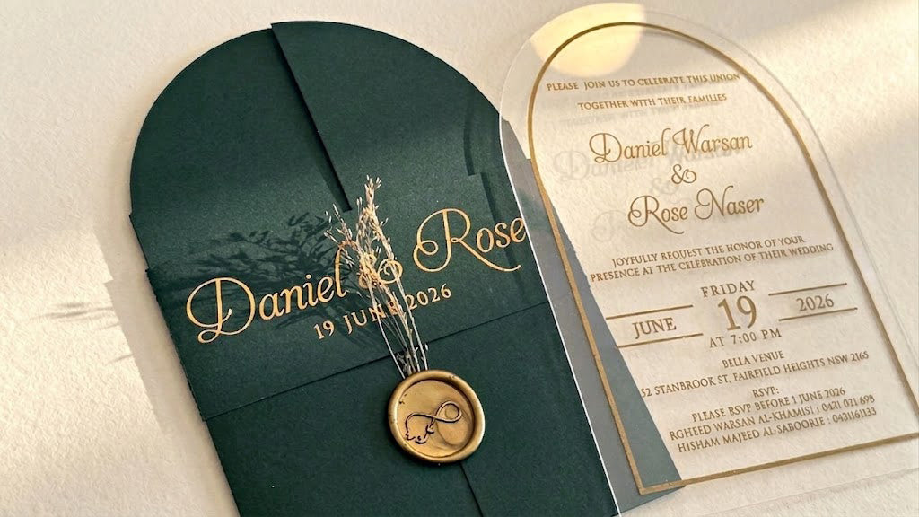 Close view of the green cover's printed paper band, dried floral stems and round wax seal, beside the arched acrylic invitation.