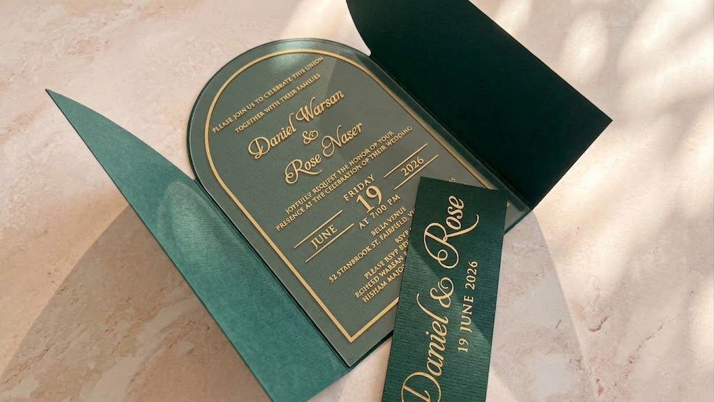 Angled view inside the open green arched gatefold cover, with the clear acrylic invitation centered and the removed printed band across the foreground.