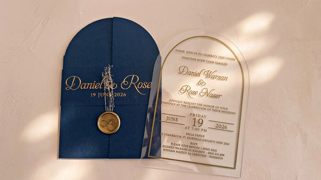 Wide front view of the navy blue arched cover and clear invitation card side by side, with soft patches of sunlight across the background.