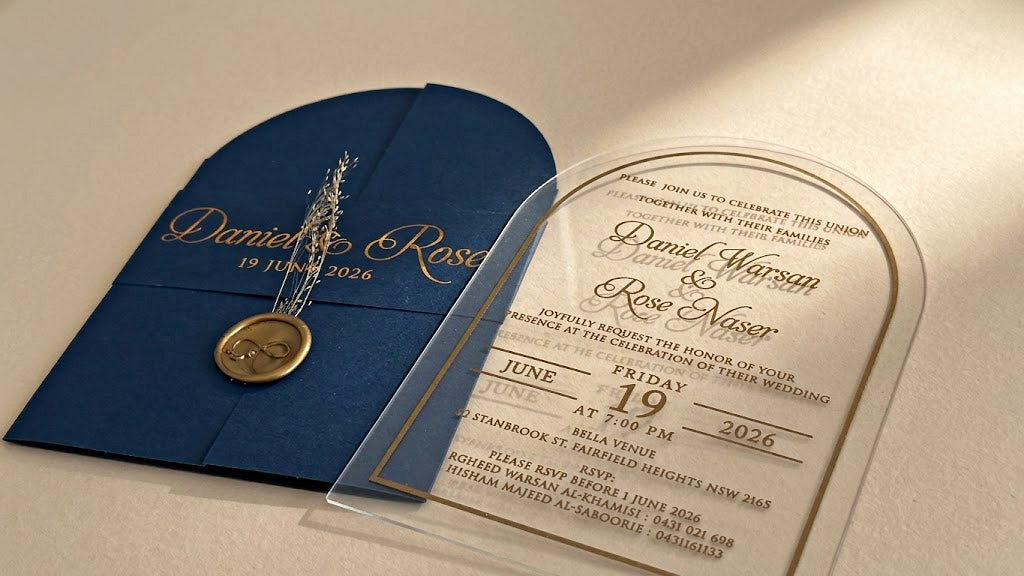 Low view of the navy blue invitation set showing the clear acrylic card's transparent outer edge and lettering beside the closed cover.