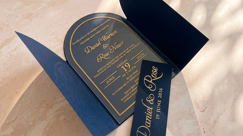 Angled view inside the open navy blue arched gatefold cover, with the clear acrylic invitation centered and the removed printed band across the foreground.