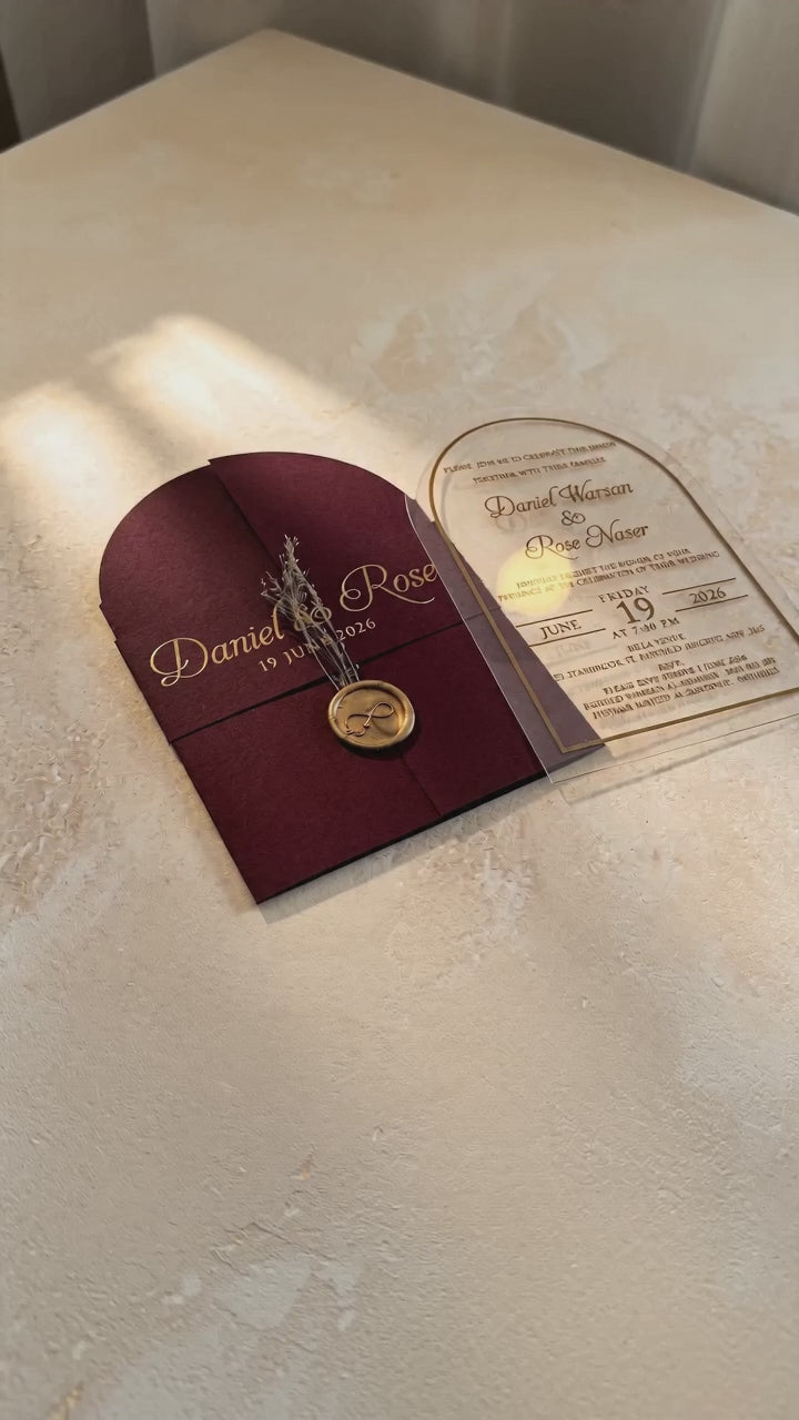 Video showing the burgundy cover's wax seal and dried flowers, then lifting and tilting the clear arched acrylic invitation to show its transparency.