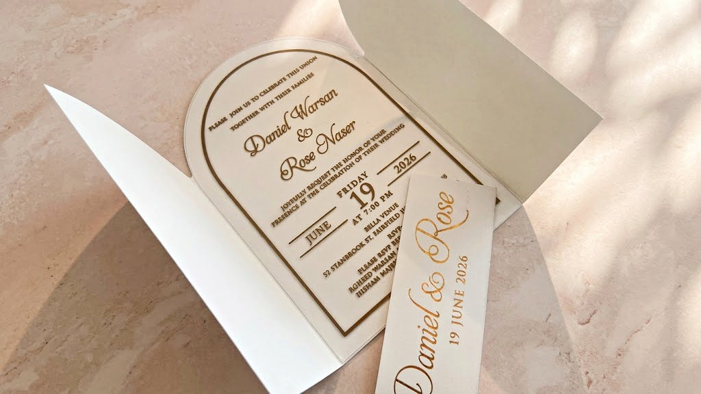 Angled view inside the open white arched gatefold cover, with the clear acrylic invitation centered and the removed printed band across the foreground.